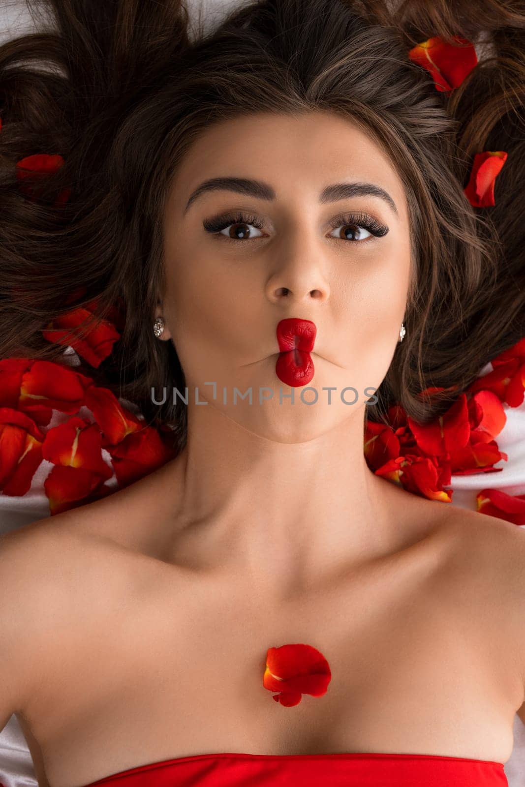 Brunette in red with emotional lips on bed with rose petals high angle portrait