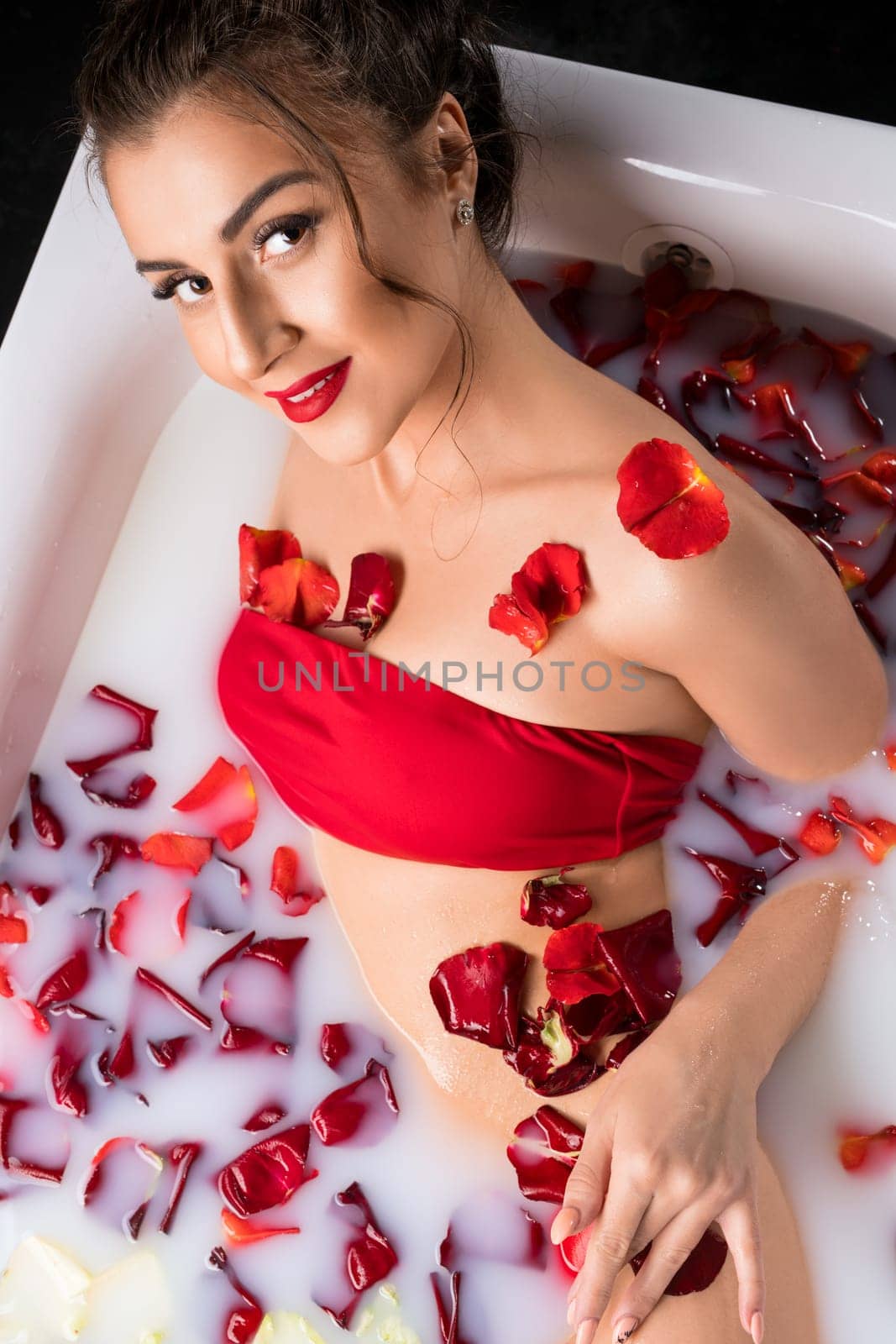 Woman in red bikini having a milk bath with rose petals high angle view