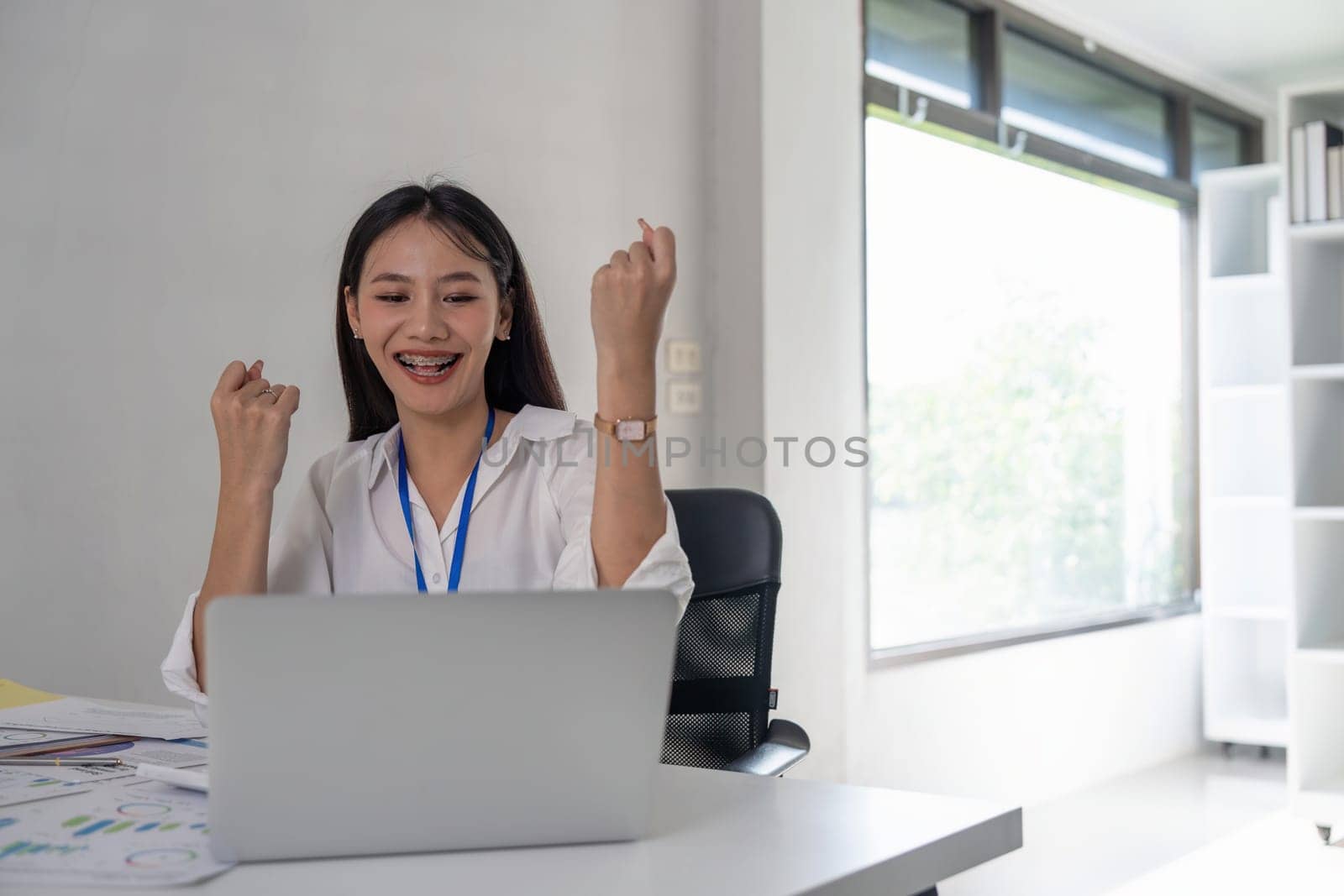 Happy excited successful Asian businesswoman triumph with a laptop computer in the workplace office by nateemee