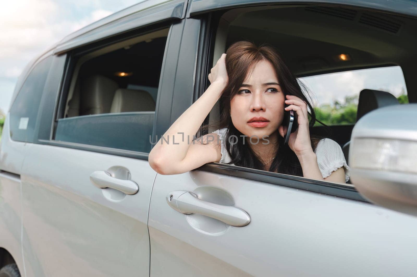 Stressed and confused Asian woman calls insurance on faulty car while traveling together by wichayada