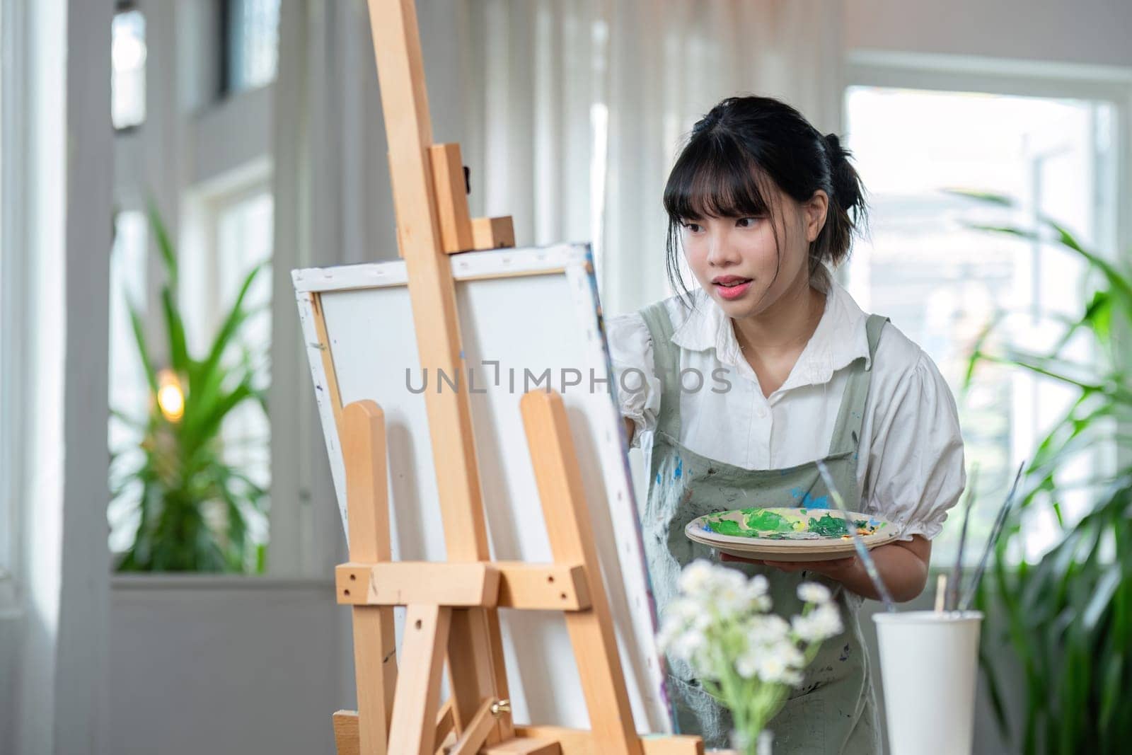 Young female artist works on abstract acrylic painting on canvas in art painting studio..