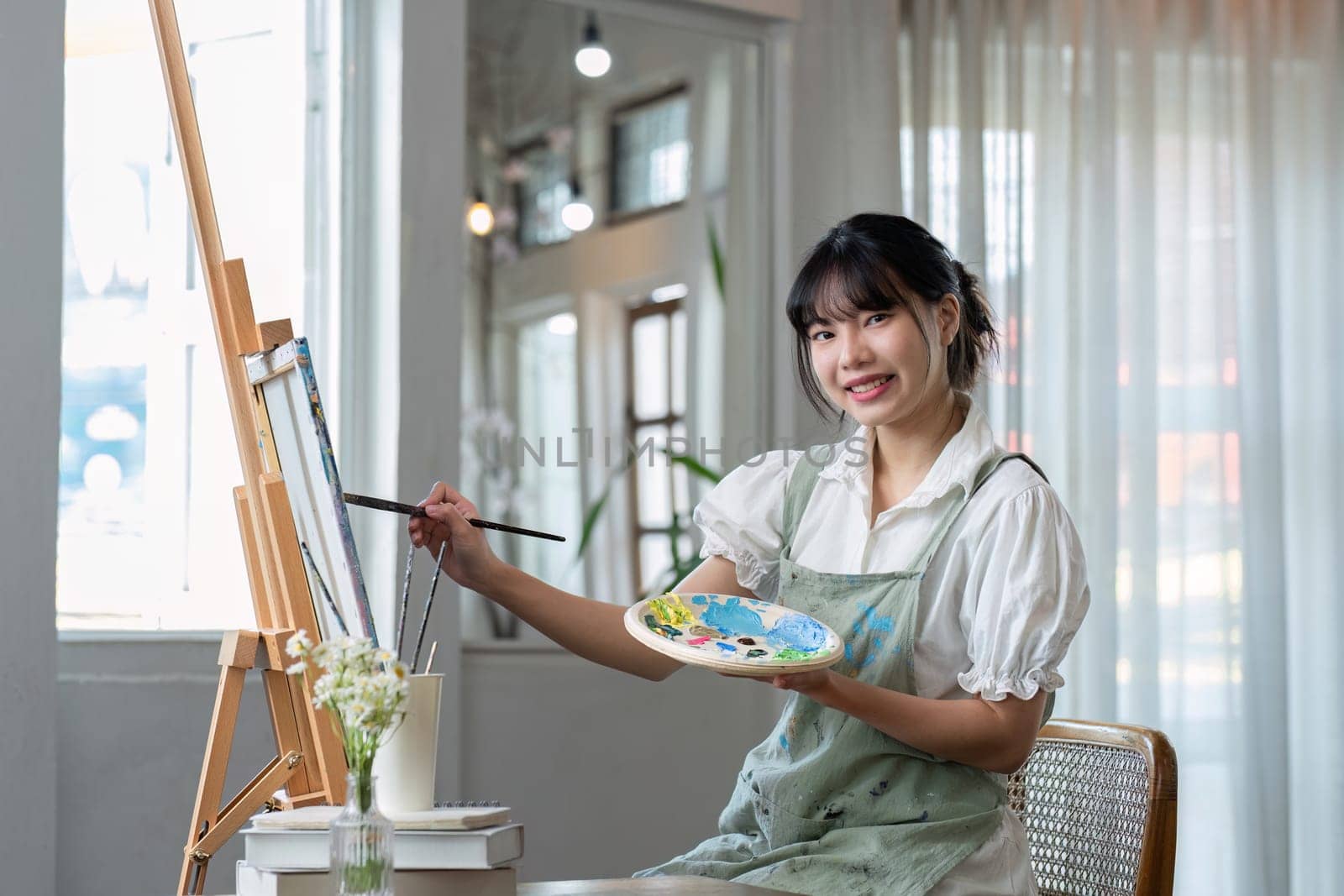 Young female artist works on abstract acrylic painting on canvas in art painting studio. by wichayada