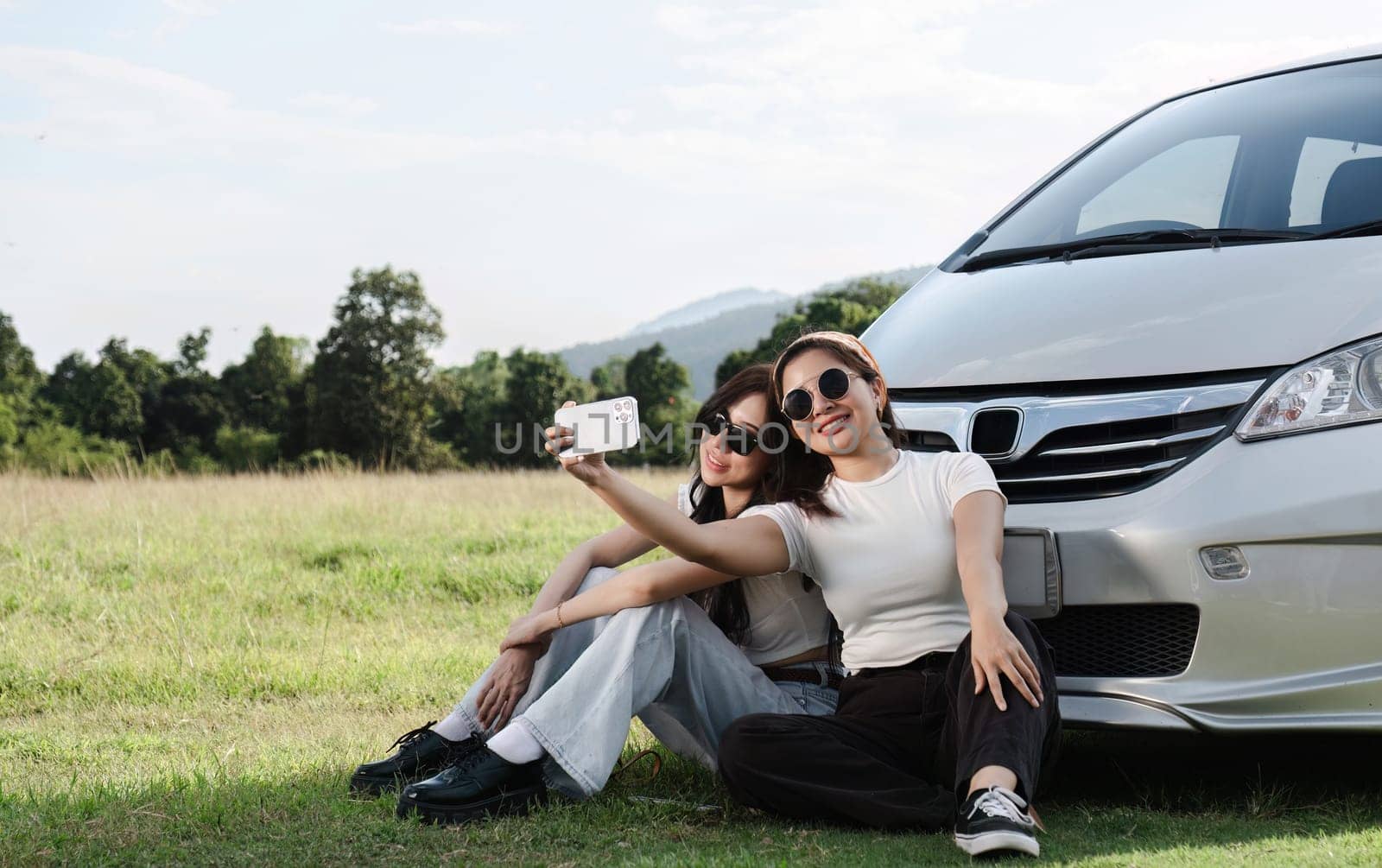 Two young women in white t-shirts and jeans sit back and relax, taking selfies together with their cell phones..