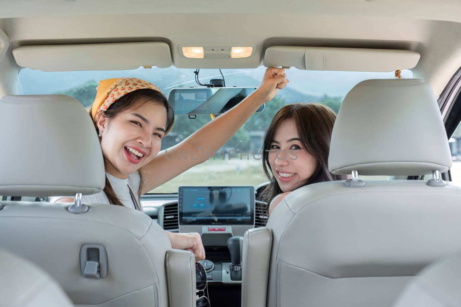 View from the back of the car of two happy beautiful cheerful women hanging out together while sitting in the car..