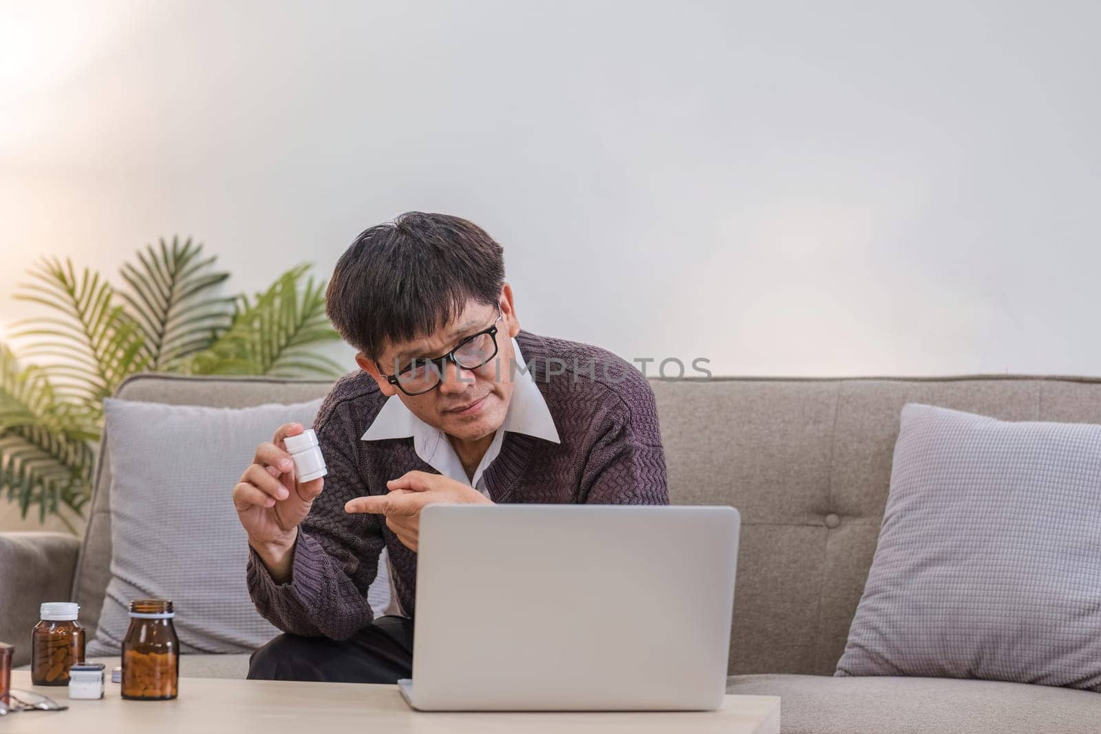 A curious elderly man holds a medicine bottle. Consult with doctor about medication use via video call. Talk to doctor. by wichayada