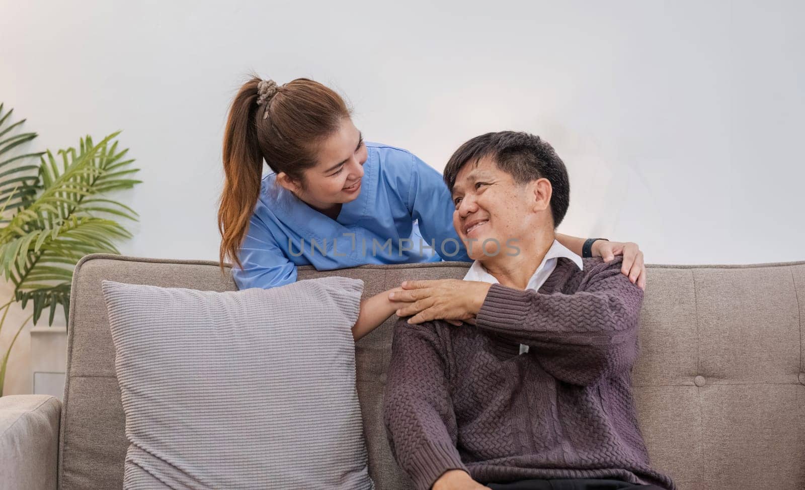 Nurse supports man during recovery A caregiver holds the hand of a senior patient who is resting in the living room and shows kindness while checking up on a retired person at home. by wichayada