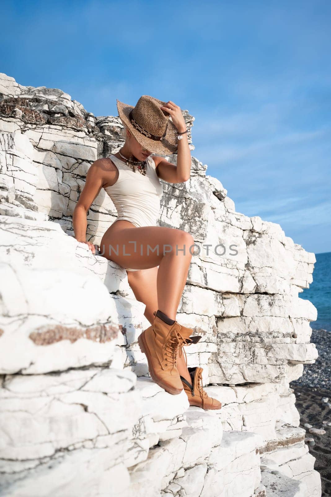 sexy girl in a bodysuit and a cowboy hat and cool boots poses freely sexually on white rocks by Rotozey