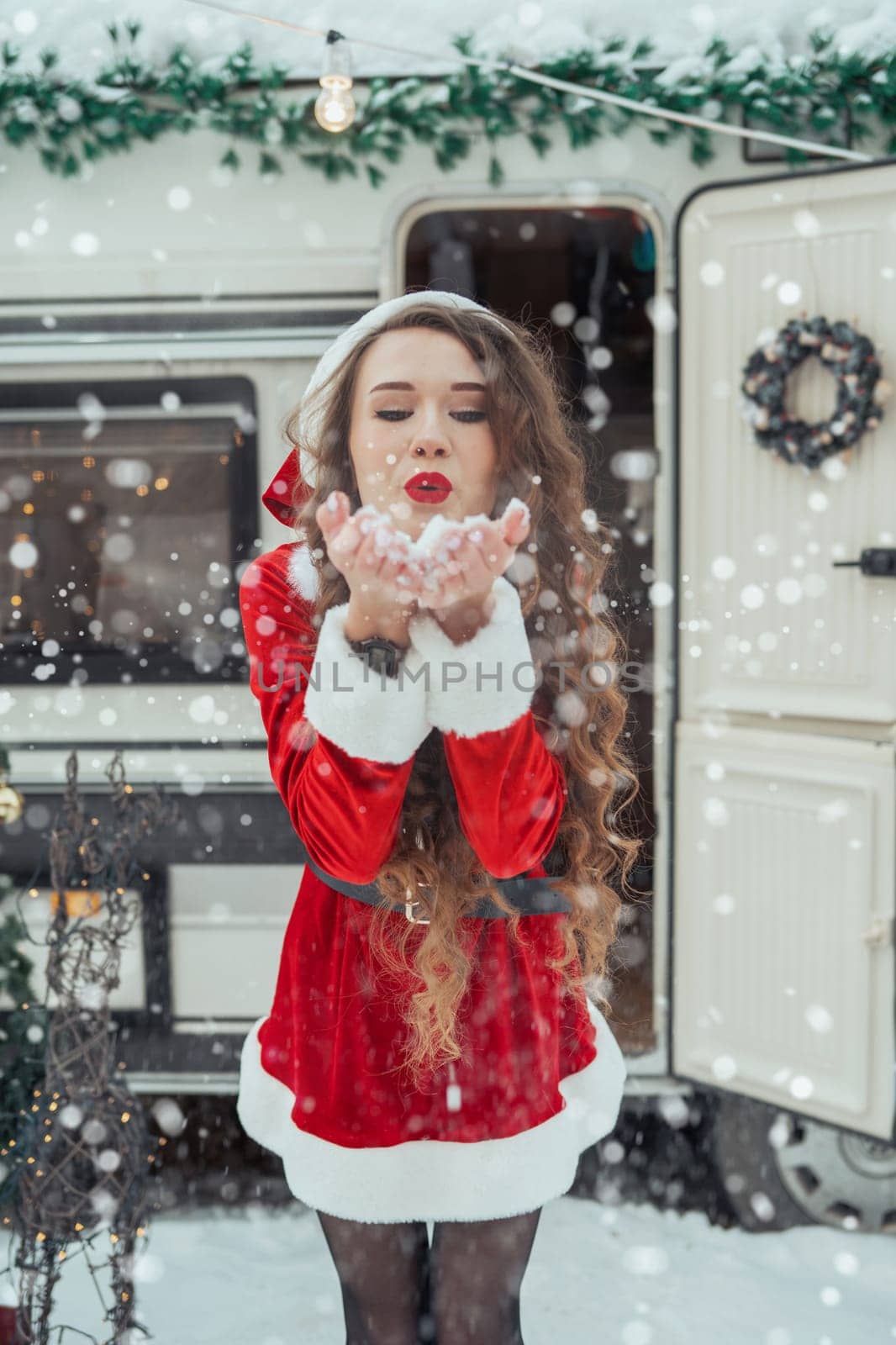 Young woman in santa costume decorates the Christmas tree at winter campsite getting ready for the new year. New year celebration concept