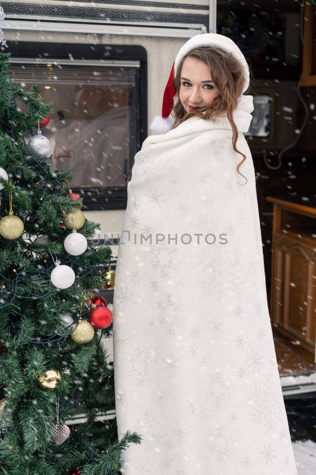 Young woman in santa costume decorates the Christmas tree at winter campsite getting ready for the new year. New year celebration concept