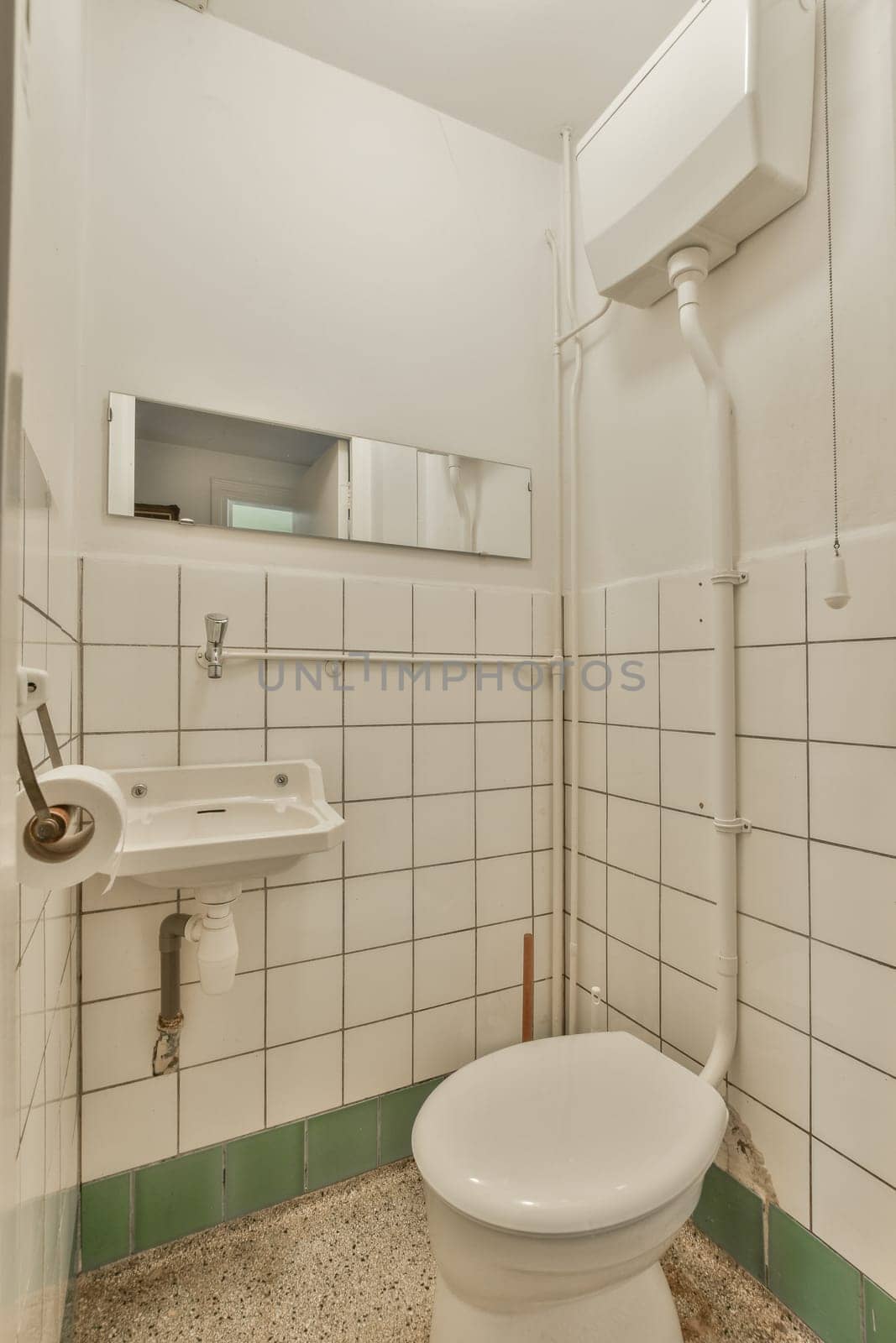 a bathroom with white tiles and green trim on the walls, along with a toilet in the center of the room