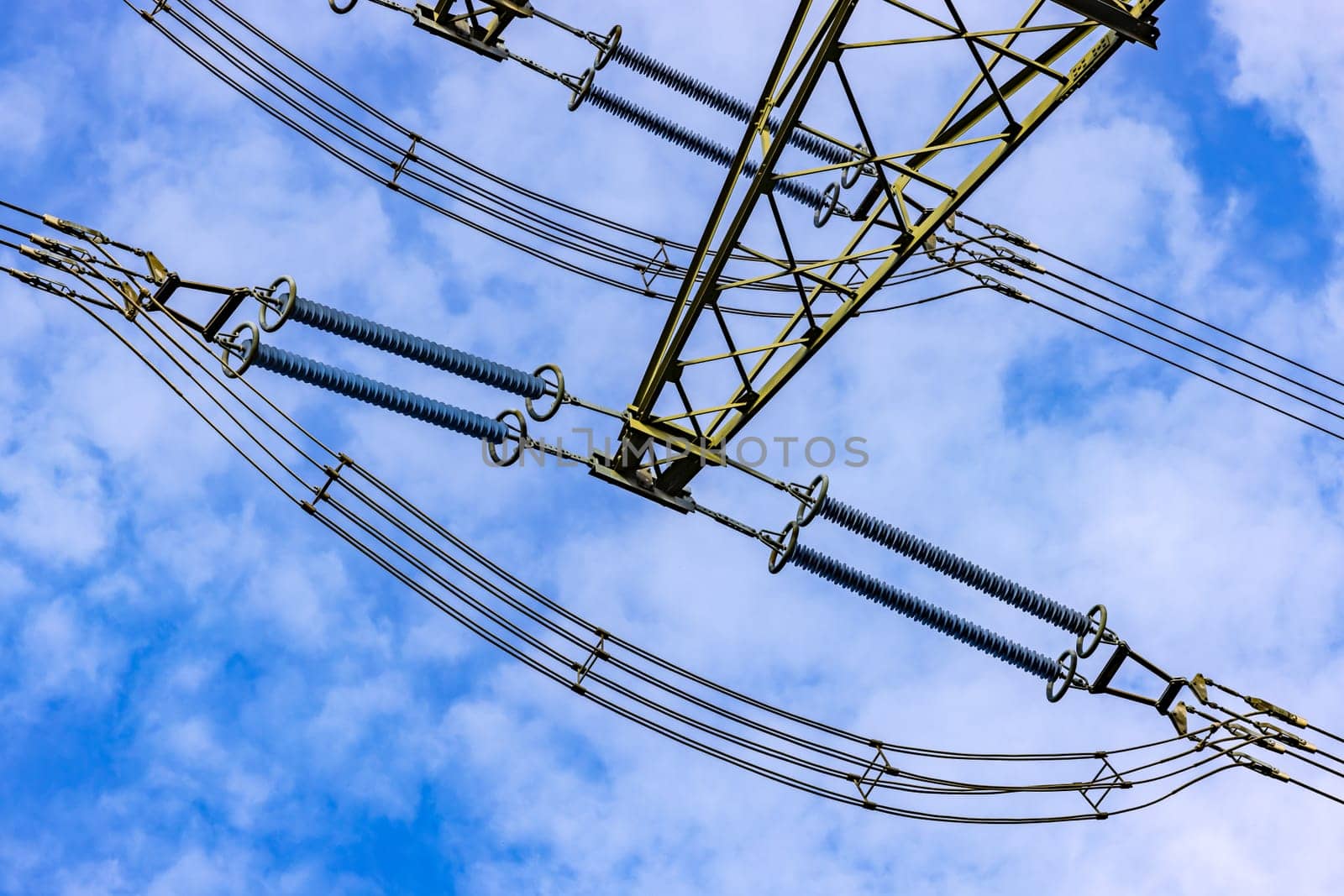 Lines for electricity with insulators and cables on a high voltage pylon as a view upwards against the blue sky