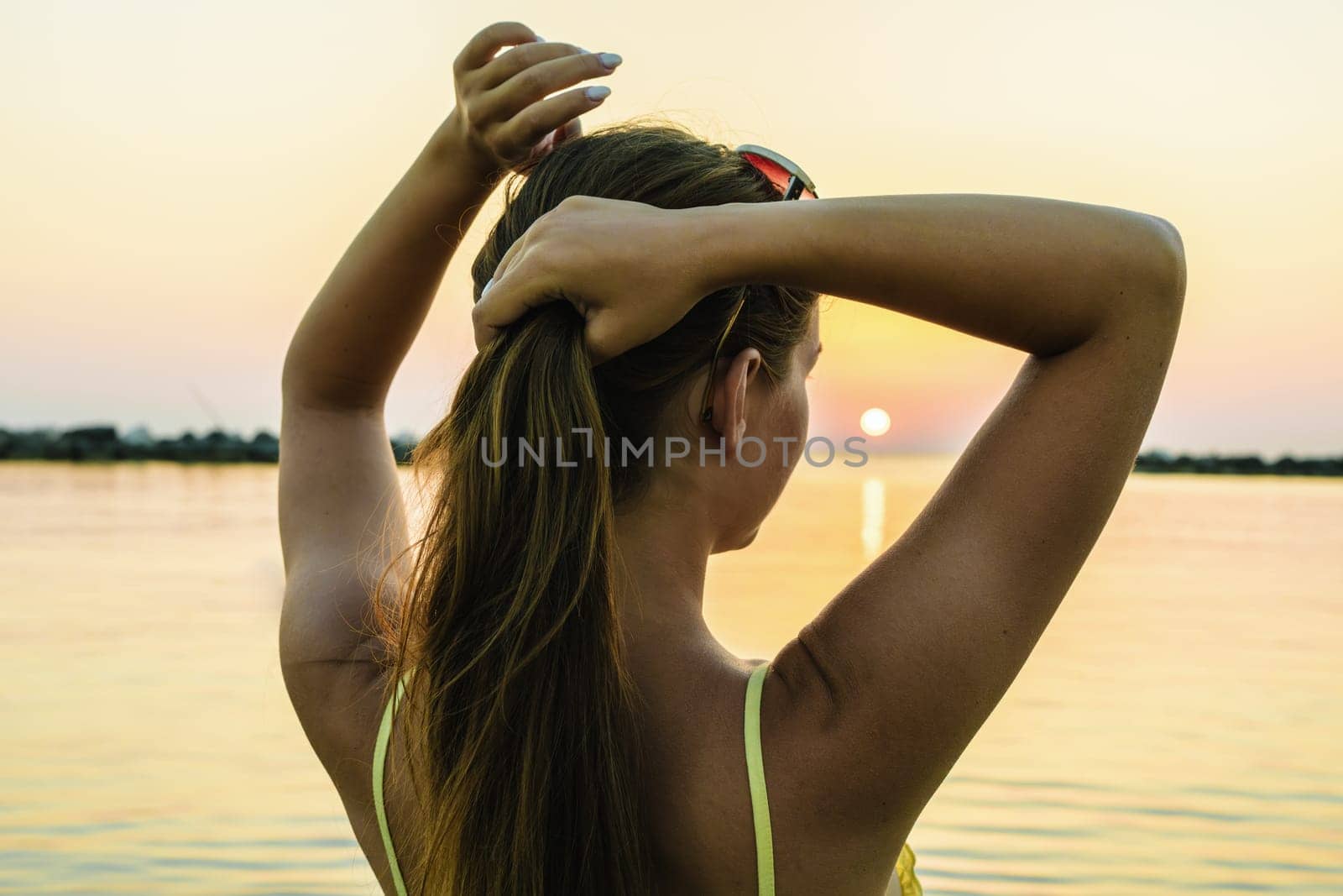 Caucasian woman standing with her back enjoying the sun on the beach during sunrise or sunset.