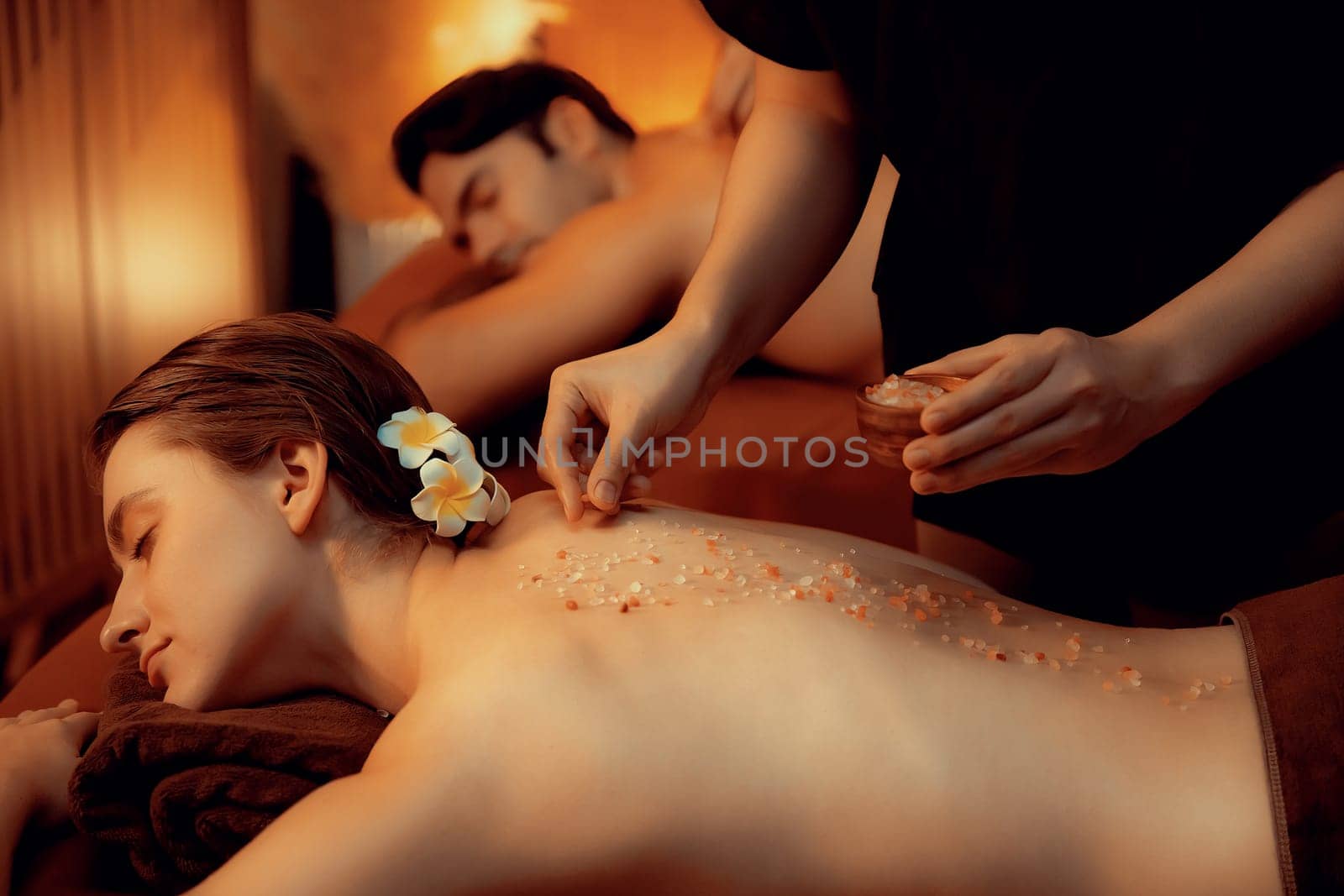 Couple customer having exfoliation treatment in luxury spa salon with warmth candle light ambient. Salt scrub beauty treatment in Health spa body scrub. Quiescent