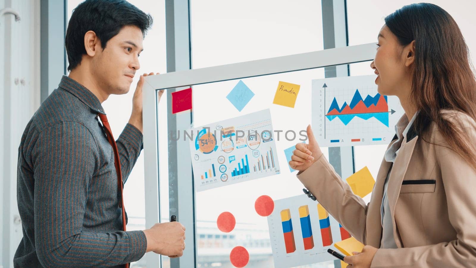 Business people work on project planning board in office and having conversation with coworker friend to analyze project development . They use sticky notes posted on glass to make it organized. Jivy