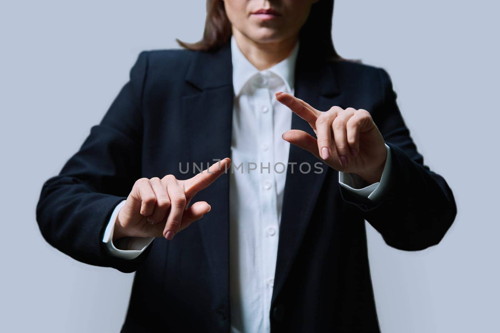 Close-up of business woman's hands using invisible touchscreen pressing key on virtual screen, on grey studio background. Business, work, profession, technology concept.