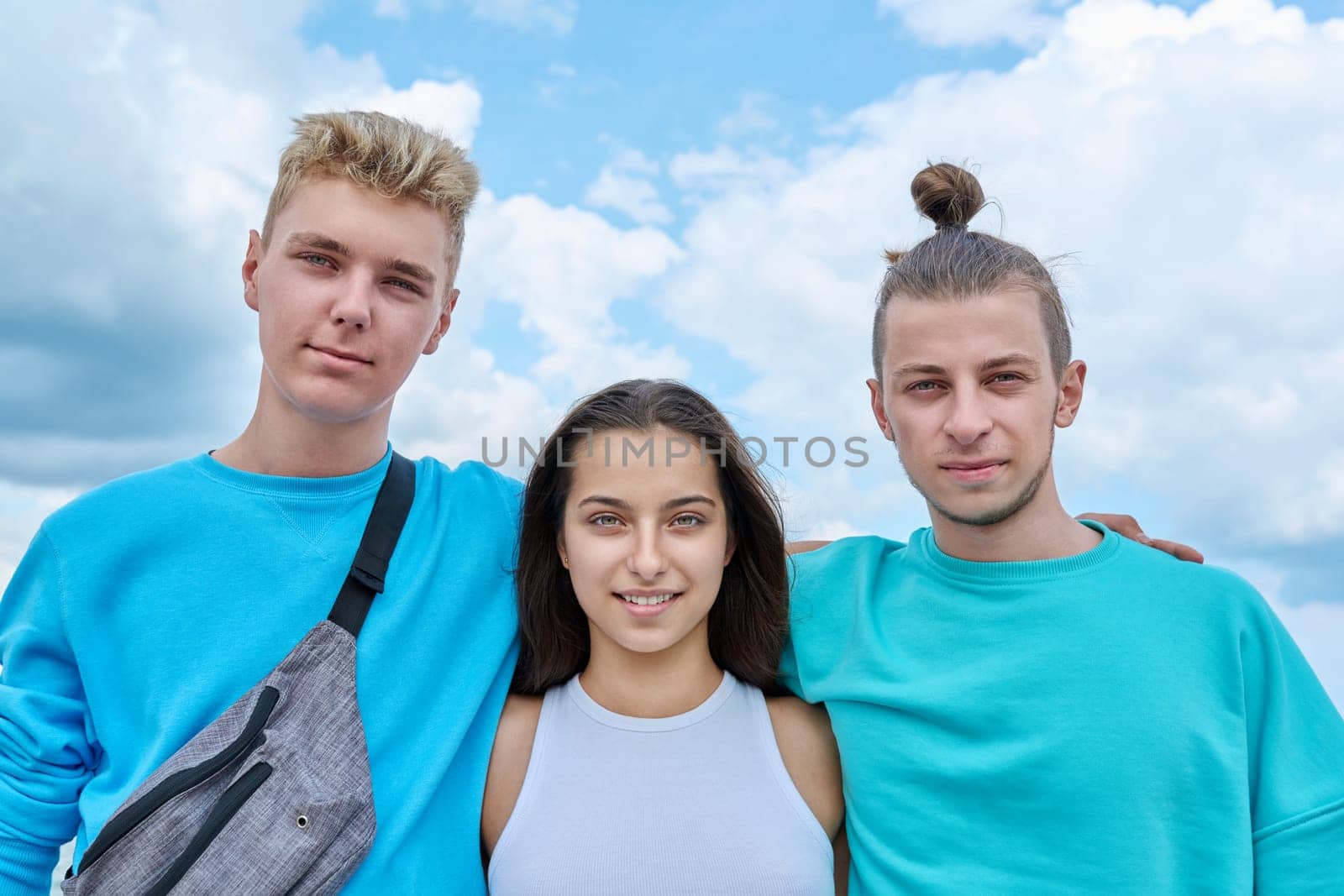 Group team of friends, teenagers guys and girl embracing looking at the camera, outdoor, sky background. Youth, summer vacation, communication, leisure, friendship, fun, lifestyle, holiday concept