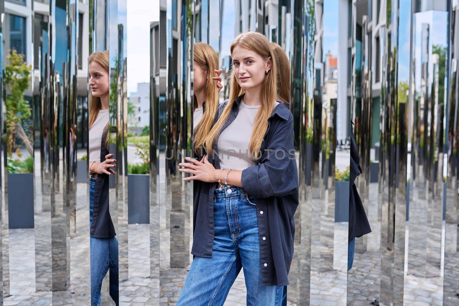 Portrait of young beautiful teenage female in modern city, fashionable smiling girl with long hair looking at camera, on mirror architecture. Beauty, fashion, youth, urban style concept