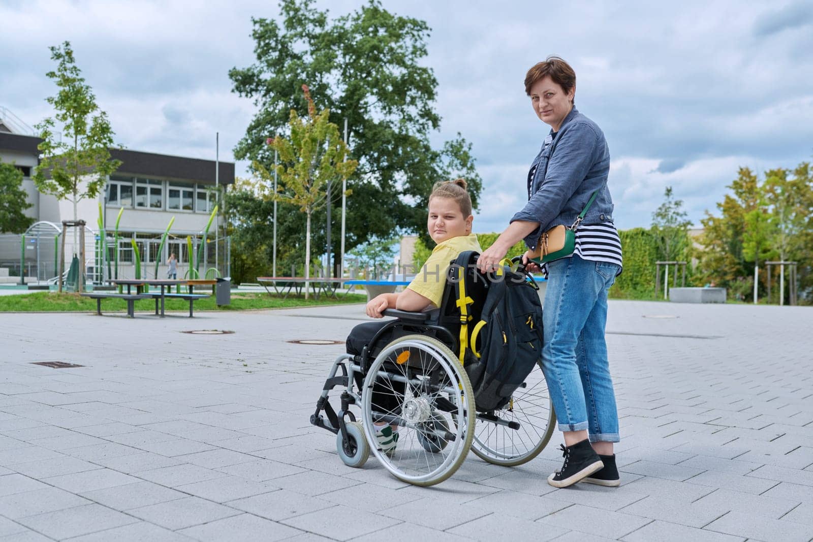 Back view of woman with boy in wheelchair near school building by VH-studio