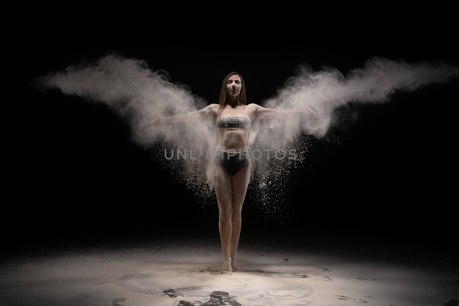 seductive brunette female in sport wear throwing dust with outstretched arms against black background