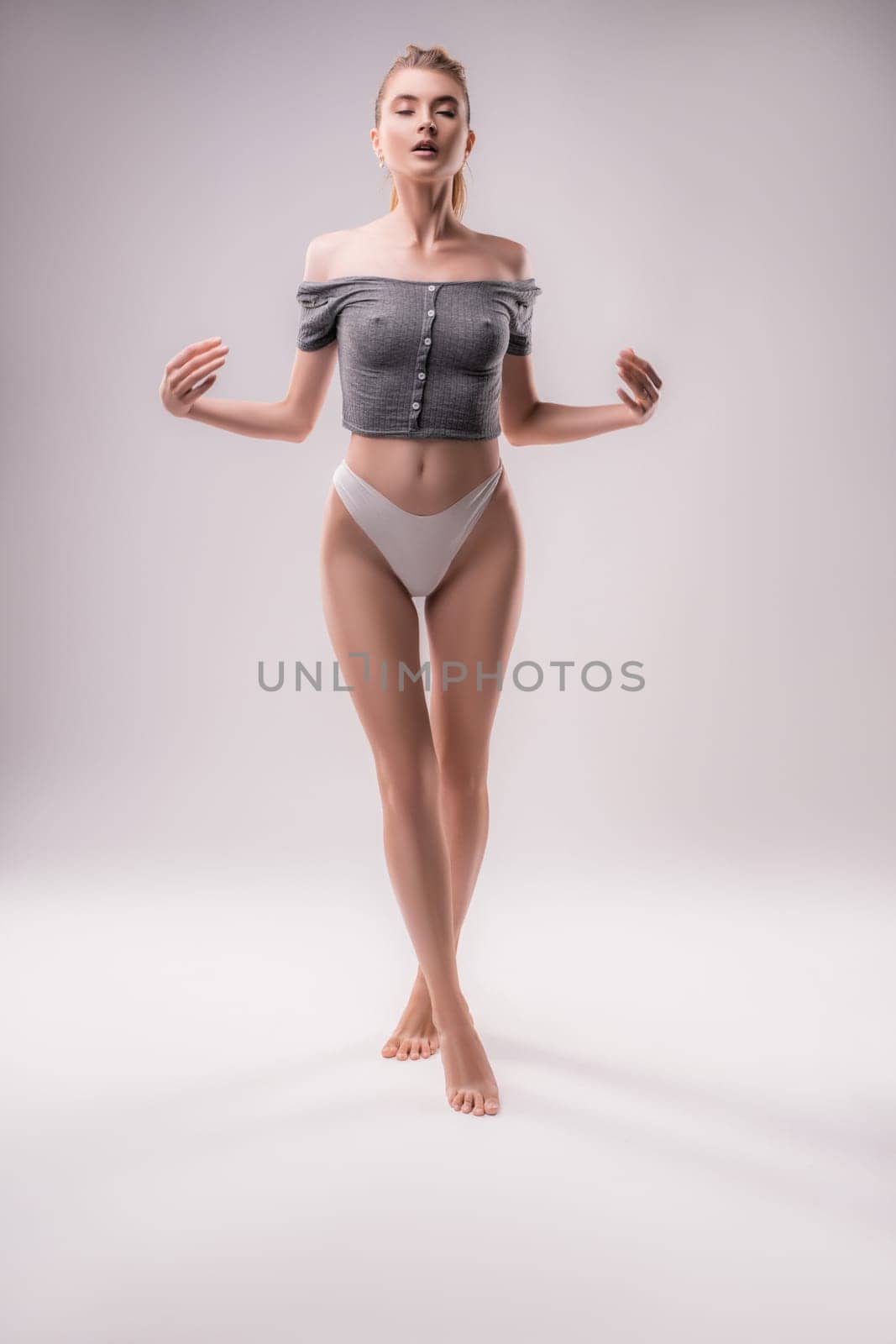 Full body of sensual female in panties standing with closed eyes in studio on white background