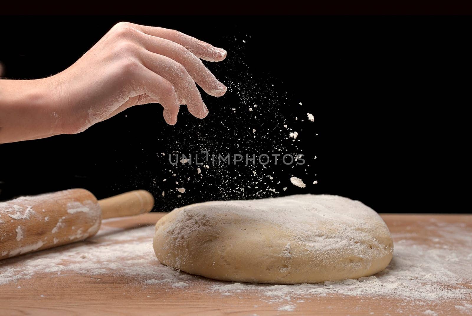 A close up of a hand sprinking flour on a piece of dough on a board.