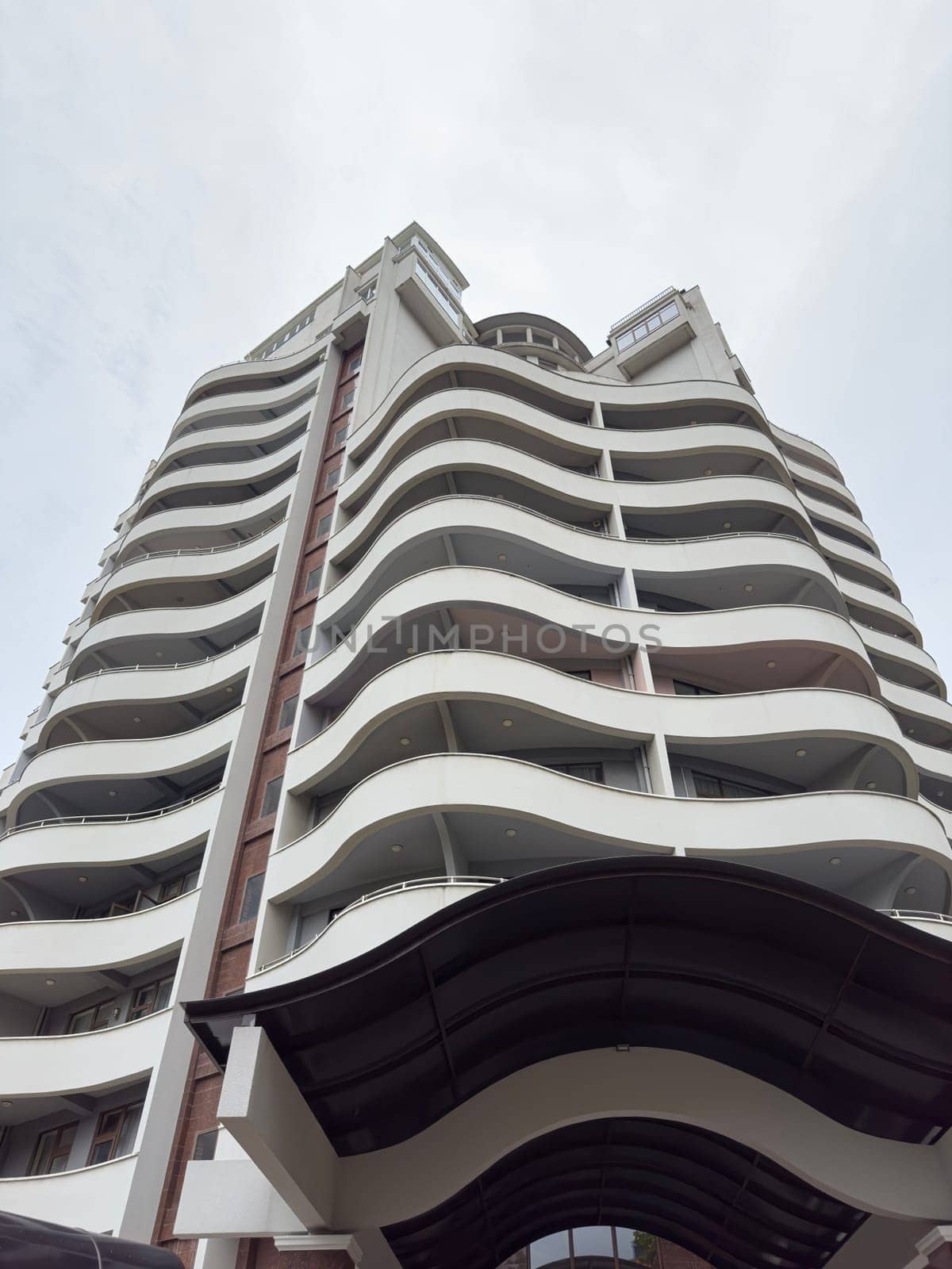 A contemporary building with flowing curved balconies rises against a cloudy sky. The structure's unique design showcases modern architecture in an urban setting.