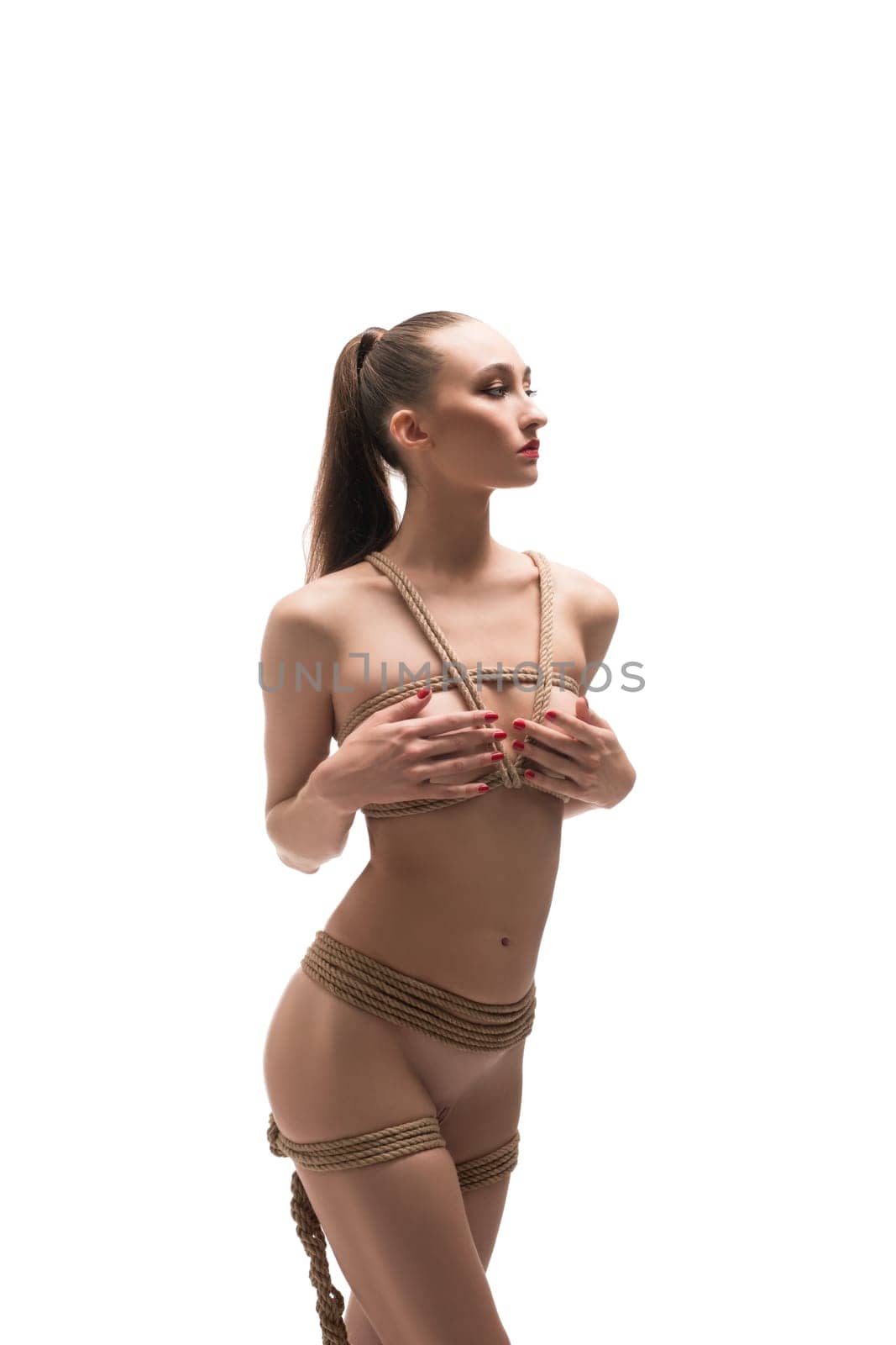 Sexy topless slim female model tied with ropes cover breast by hands isolated
