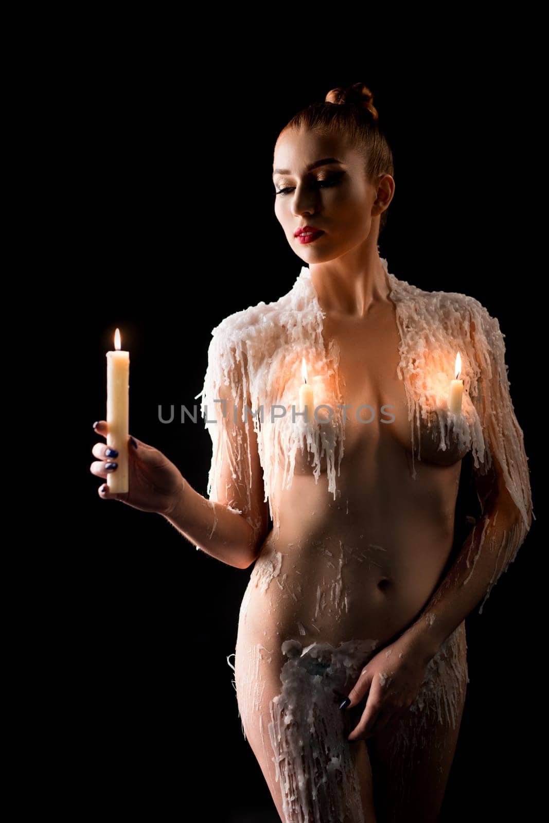 Nude female model with wax on shoulders Look at carrying burning candle on black background