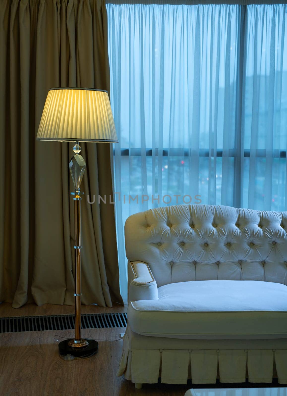Cozy atmosphere of interior of hotel room with luxury couch and illuminating floor lamp