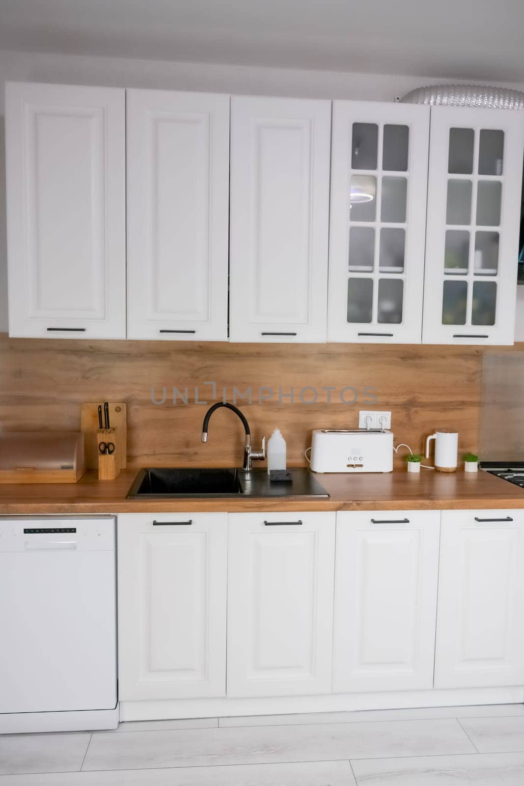 Horizontal photo of a modern kitchen in white and wooden style, in the center is a black kitchen sink, on a wooden countertop there are white wooden appliances for storing and preparing food. Modern kitchen concept, kitchen island, modern kitchen style. High quality photo