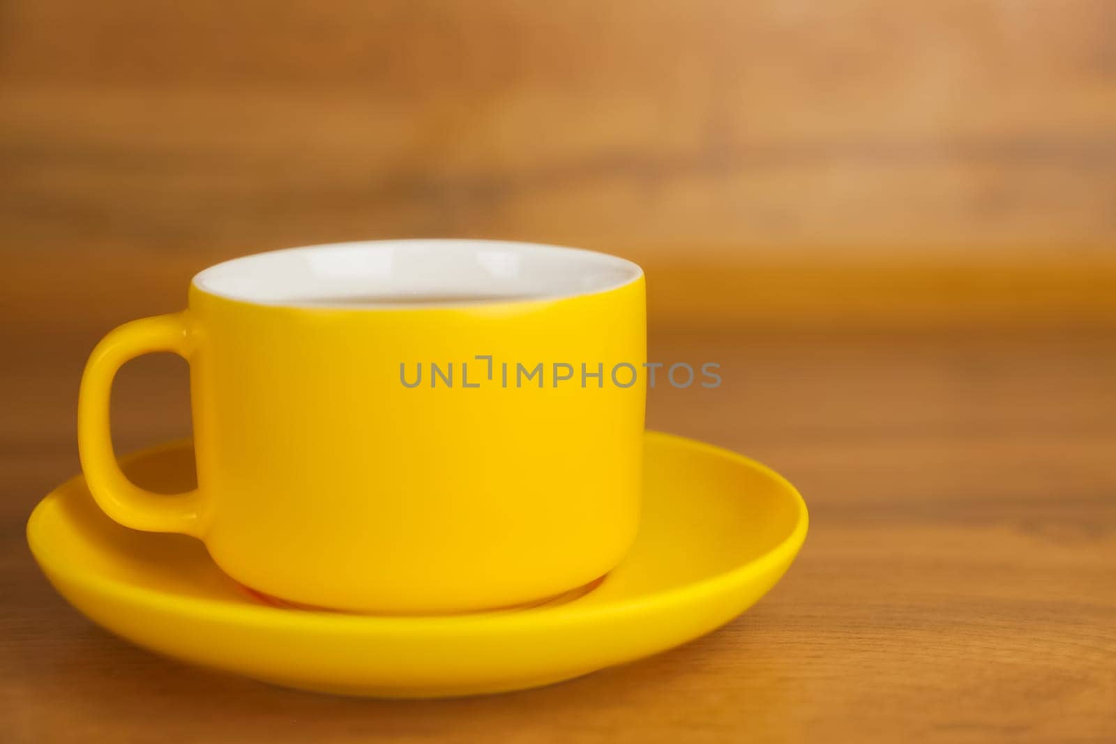 Side view of a yellow cup with a saucer in which a hot drink is poured stands on a wooden table on the left with space for text. Concept of tea drinking, cleaning break, rest. High quality photo