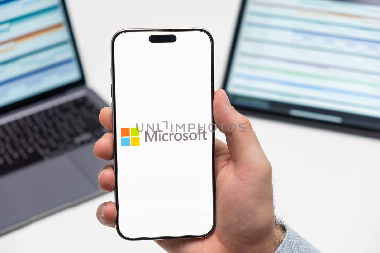 PRAGUE, CZECHIA - JULY, 2024: Microsoft logo on the screen of smartphone in mans hand and laptop on the background