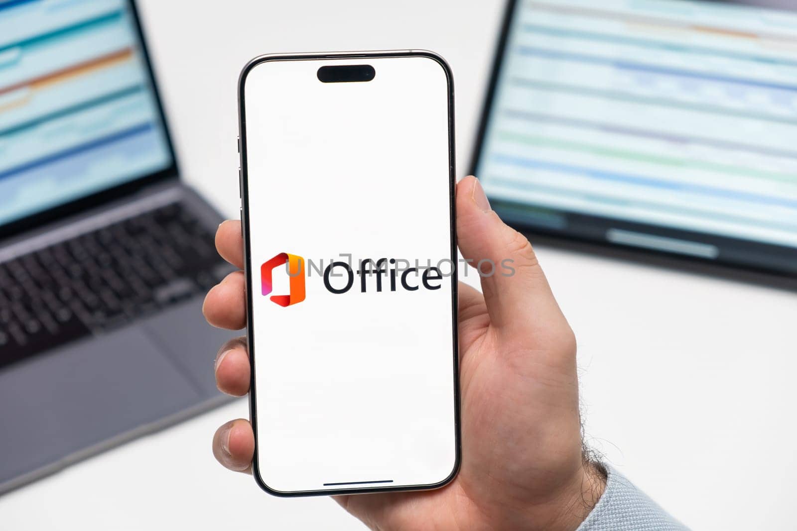 PRAGUE, CZECHIA - JULY, 2024: Microsoft Office 365 logo on the screen of smartphone in mans hand and laptop on the background
