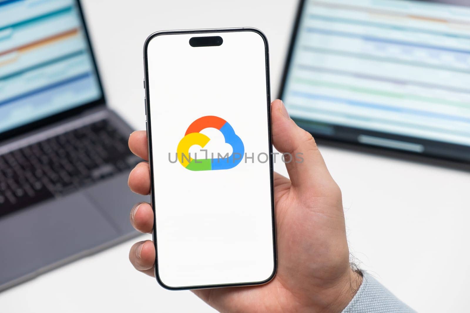 PRAGUE, CZECHIA - JULY, 2024: Google cloud logo on the screen of smartphone in mans hand and laptop on the background
