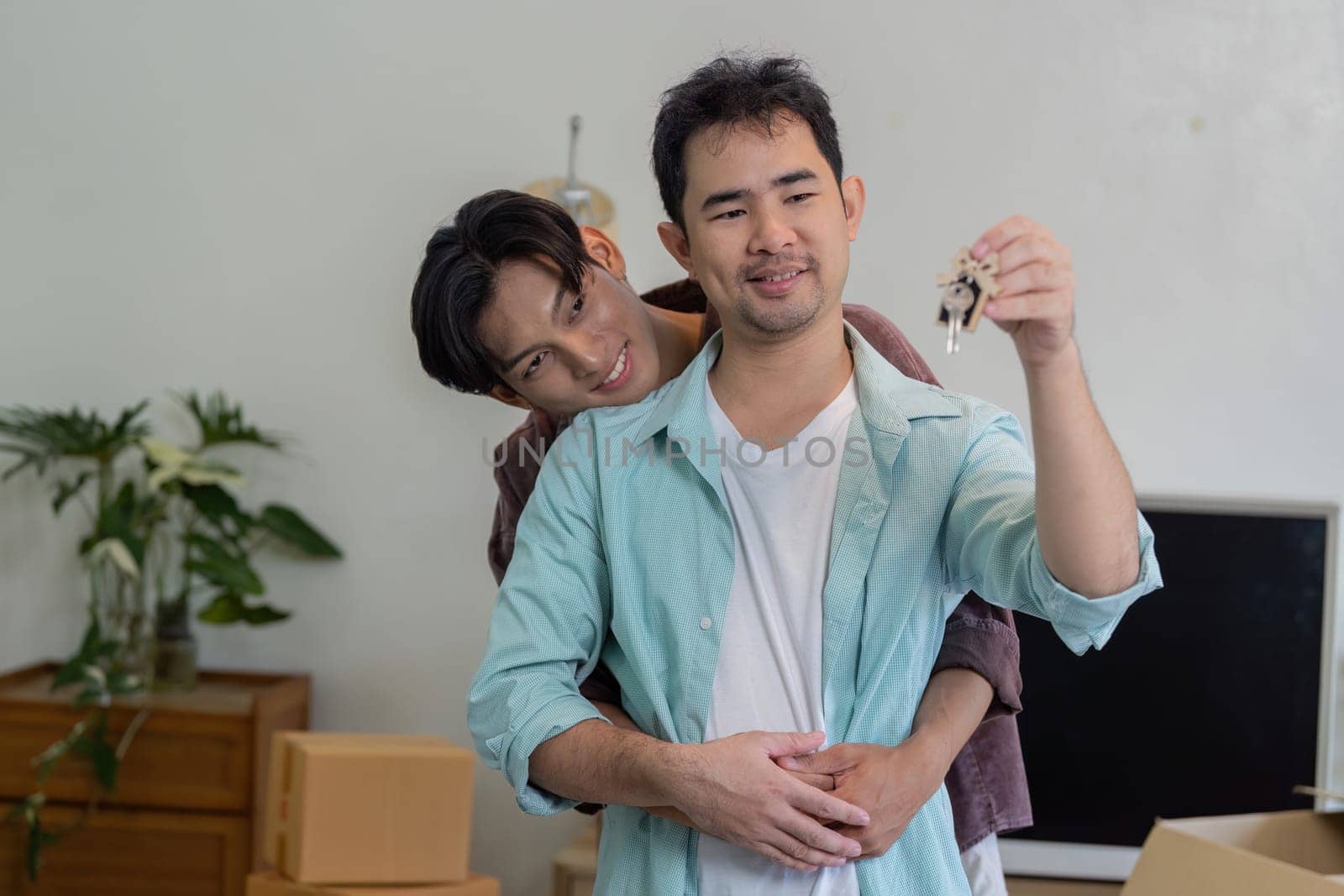 A gay couple happily embracing while holding keys to their new home, symbolizing a fresh start and love.