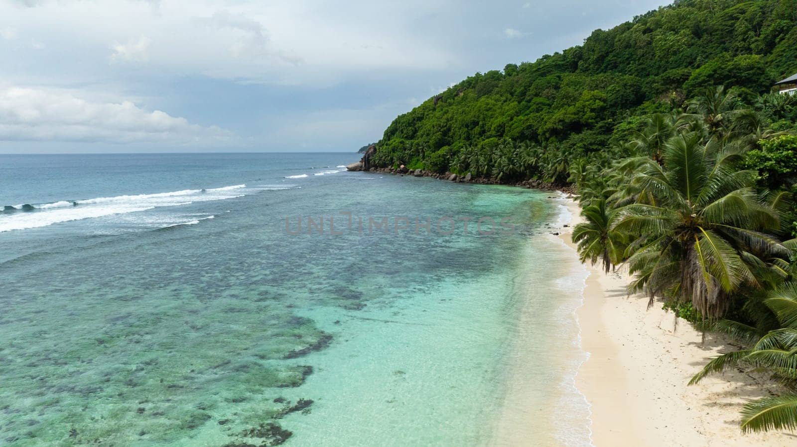 A calm bay with crystal-clear waters surrounded by dense forest and a pristine sandy shore. Mahe, Seychelles.