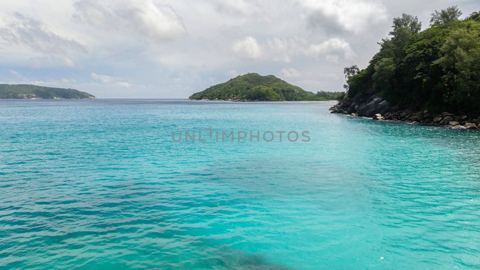 Turquoise waters embrace lush green islands under overcast sky. Seychelles, Mahe.