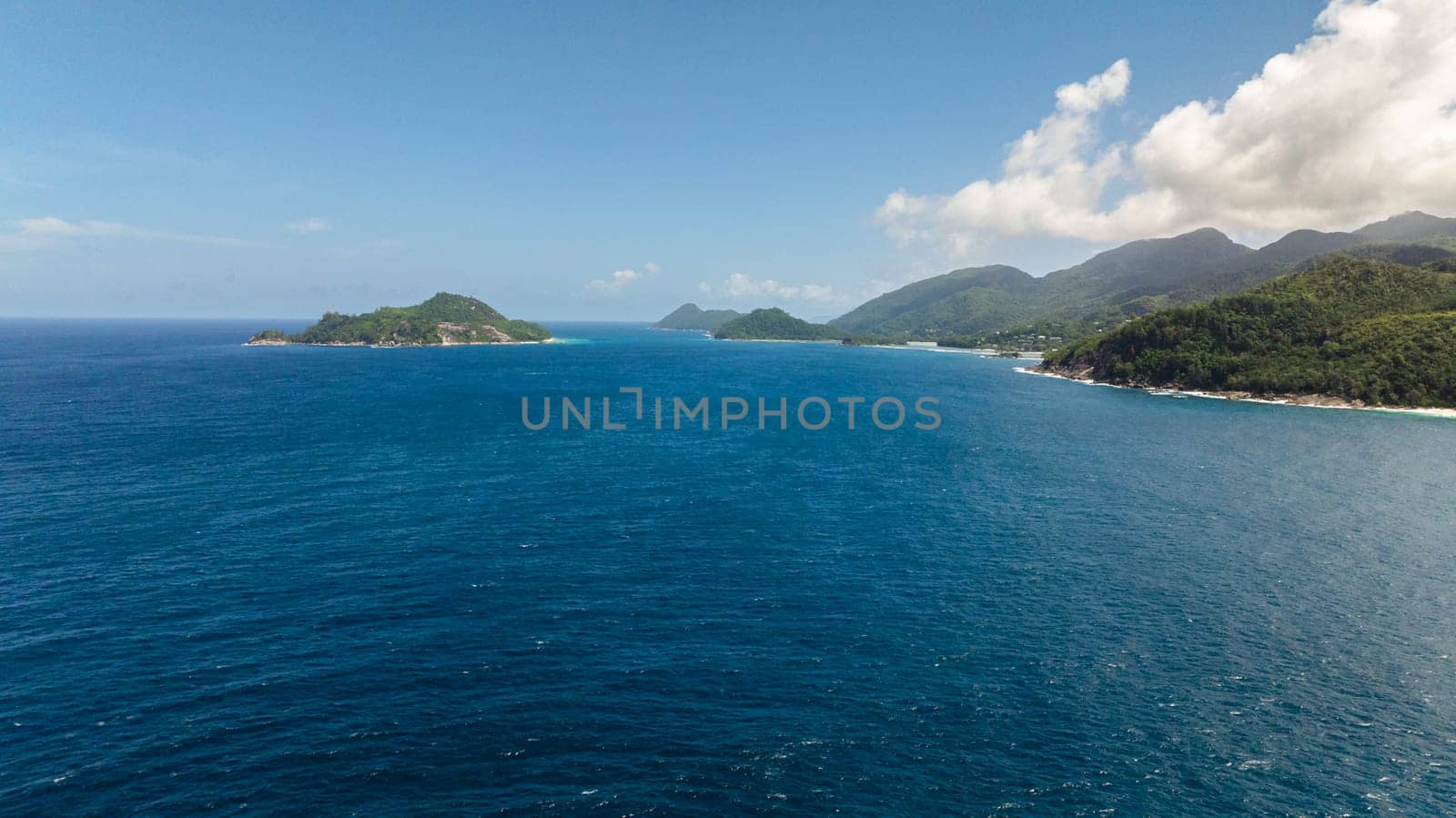 Granite boulders and ocean surf, set against a backdrop of verdant tropical forest. Seychelles, Mahe.