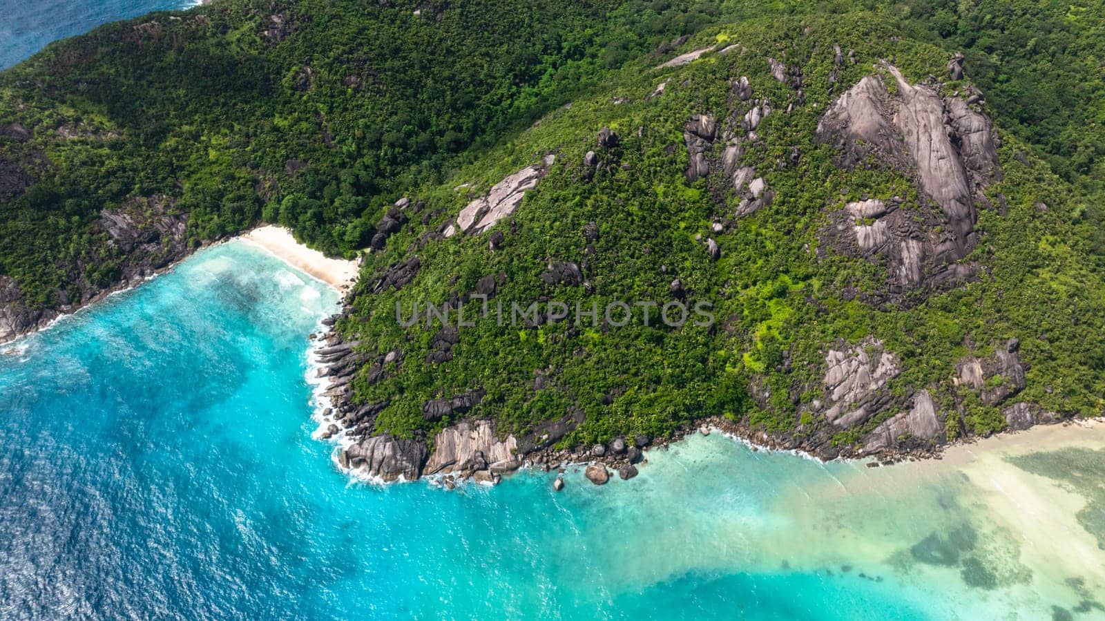 Aerial view of a tropical beach with turquoise waters, surrounded by lush green hills. Seychelles, Mahe. Anse Du Riz beach. Baie Ternay Marine National Park.