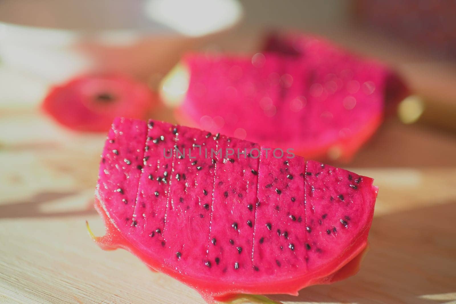 Bright pink dragon fruit slices placed on a light wood background.