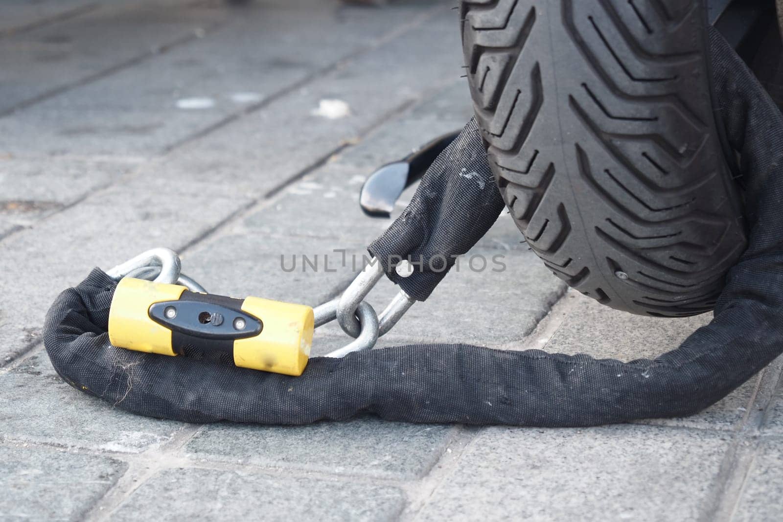 A thick cable lock connects a vehicle tire to the ground on pavement.