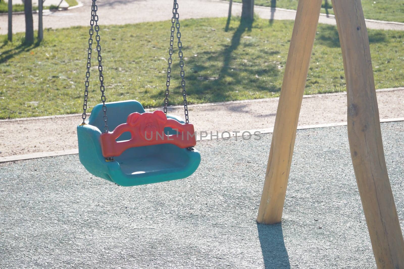 A colorful swing hangs in a lively playground under blue skies.