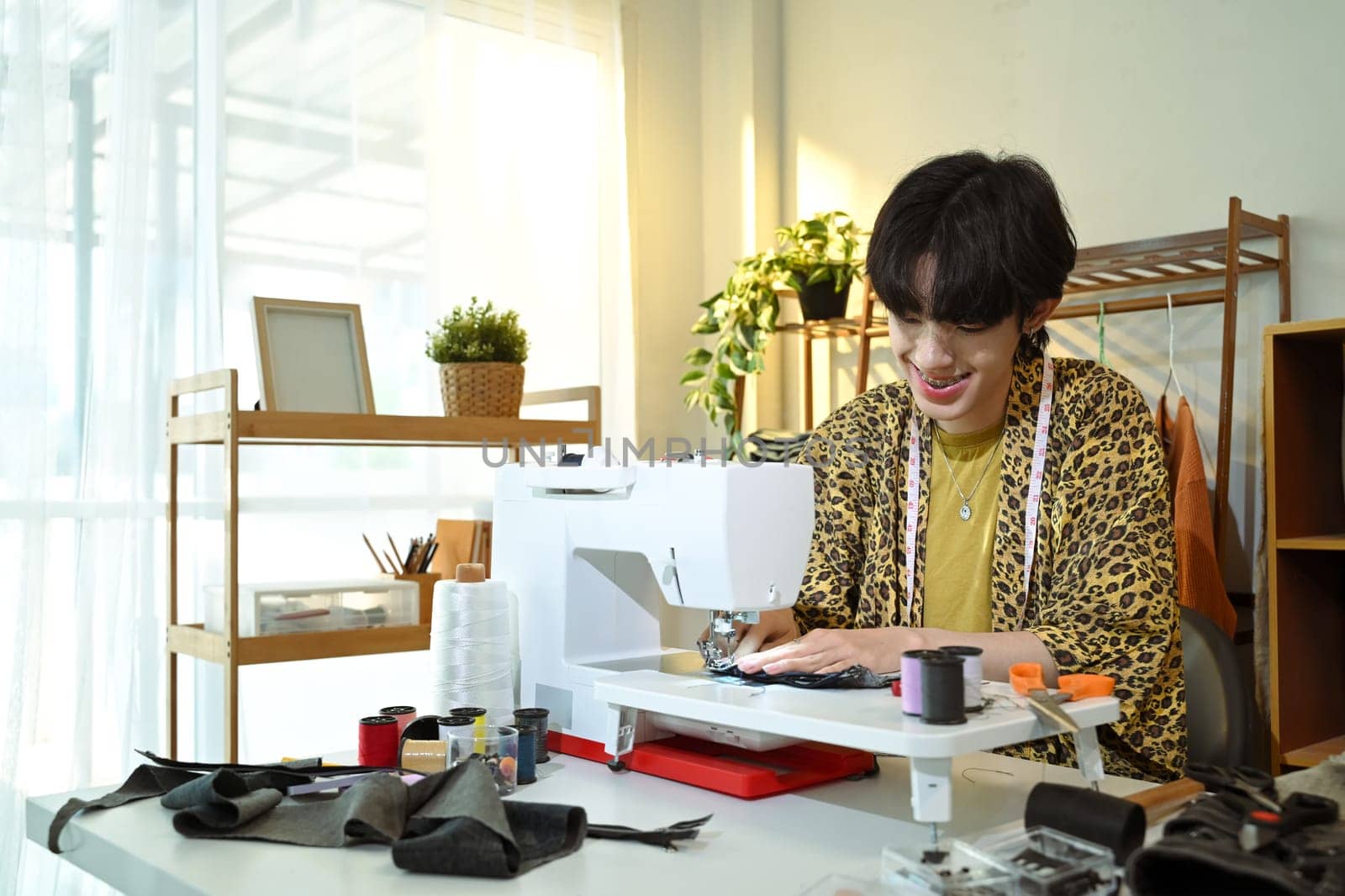 Smiling young designer working on sewing machine in a creative workspace.