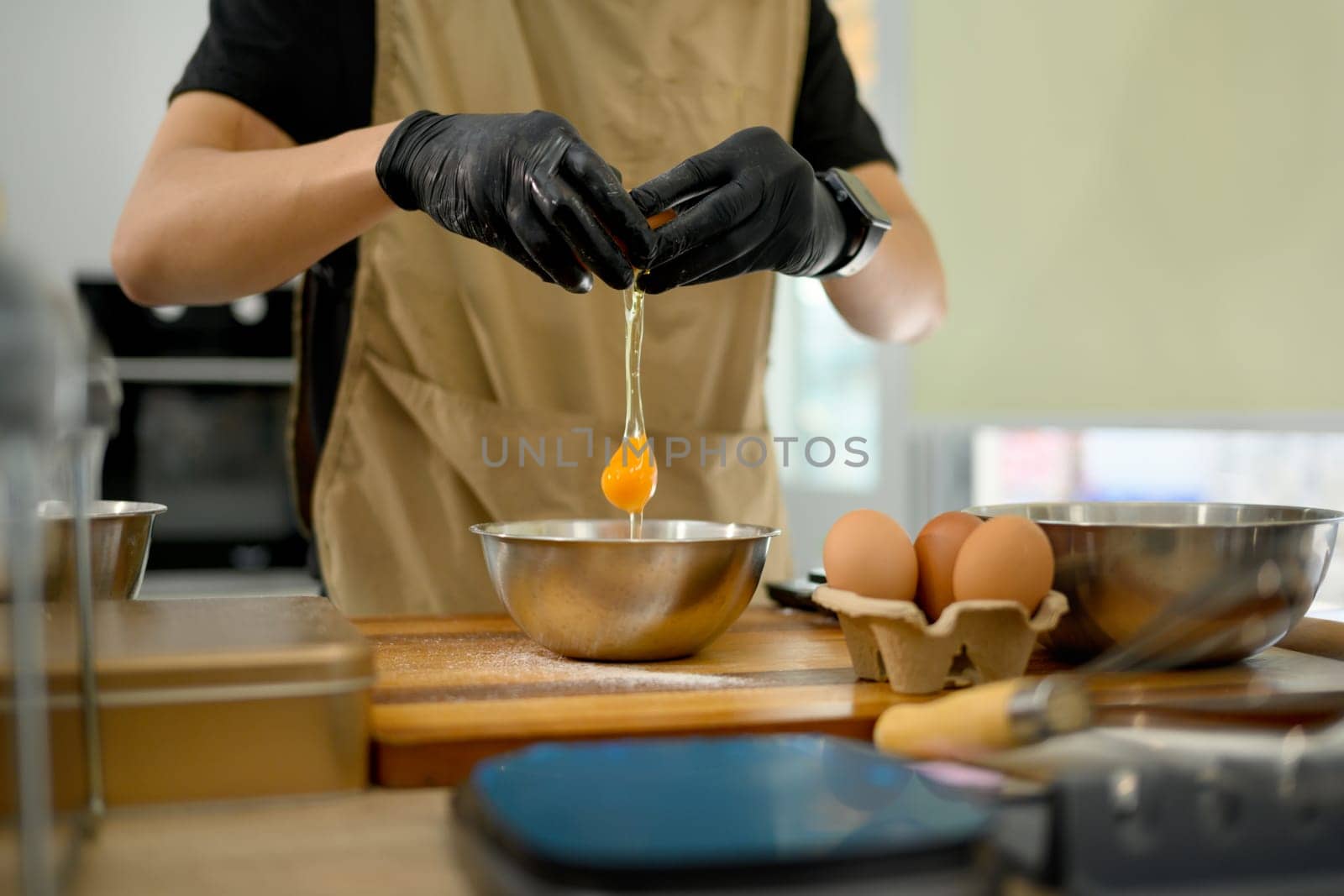 Male baker cracking an egg into mixing bowl preparing ingredients for homemade cookies.