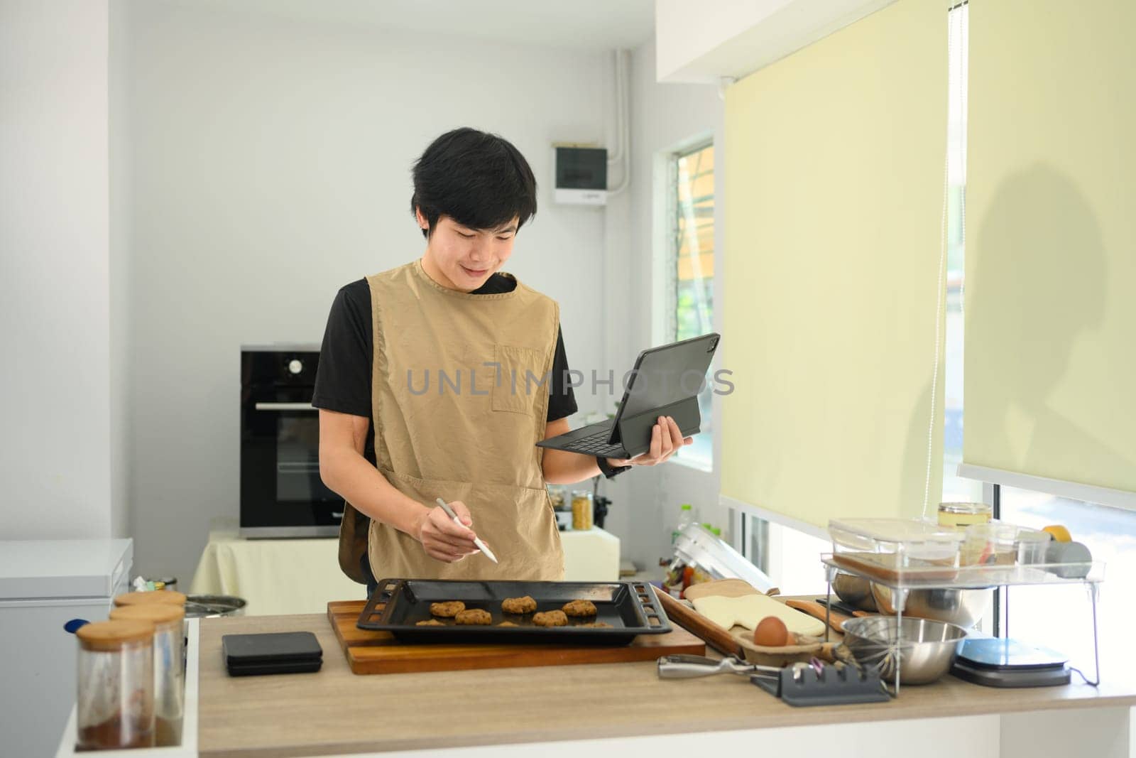 Smiling male baker checking recipe on digital tablet while preparing chocolate chip cookies.