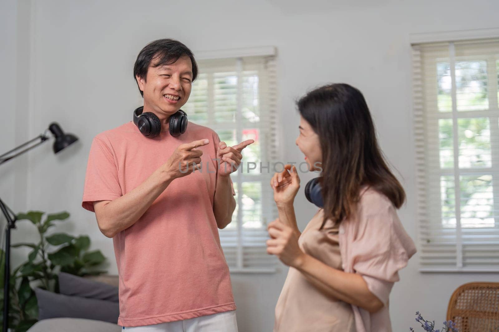 A diverse couple enjoying their time together, dancing and smiling in a cozy living room while wearing headphones.