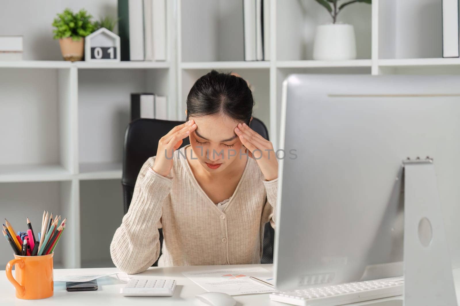 A woman experiencing stress and headache while working at her computer desk, reflecting the challenges of office syndrome in a modern workspace.