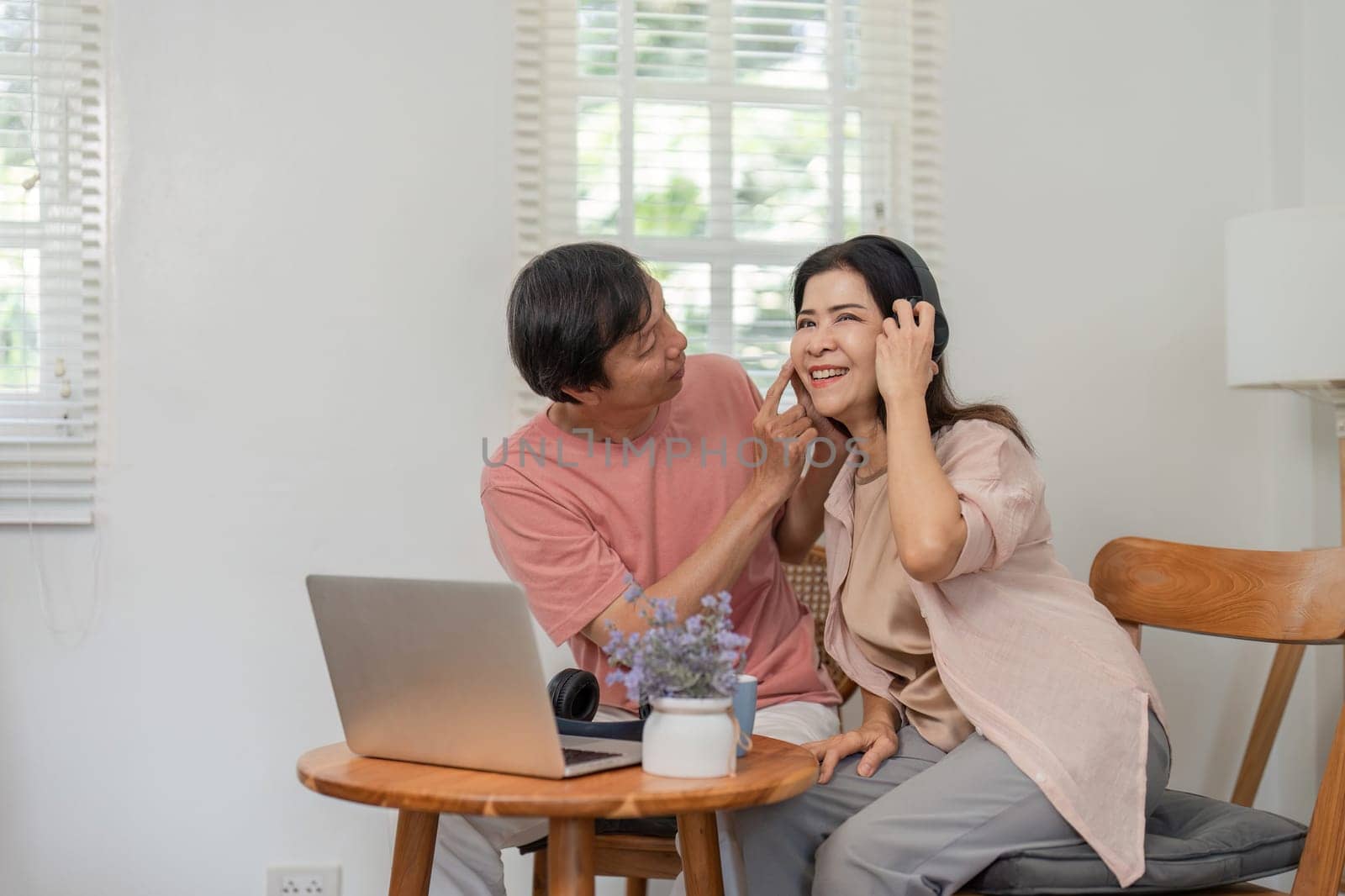 An older couple shares a moment of affection, smiling and playfully interacting while using a laptop in their cozy home environment.
