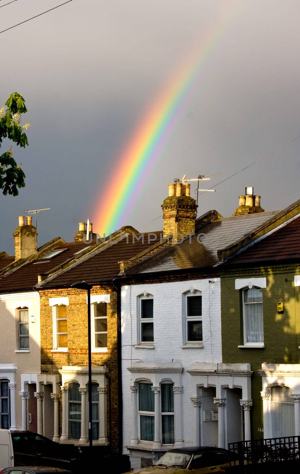 A vibrant rainbow emerges from the stormy skies above terraced houses after a rainfall, London, UK.