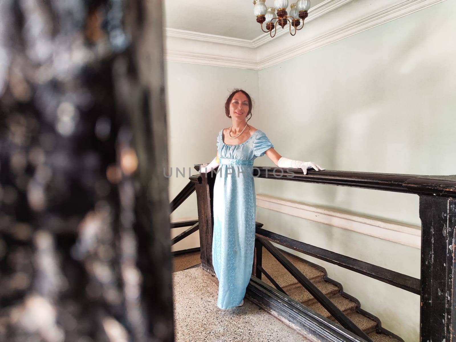 The girl dressed as a romantic princess presents a graceful pose in the ancient castles staircase, embodying a vintage aesthetic.
